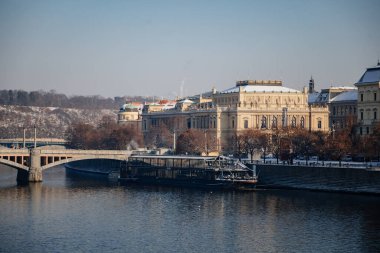 Prague, Czech Republic, 15 December 2022: Old town with towers above River Vltava, View from Charles bridge, snow on roof at sunny winter day, UNESCO, concert hall Rudolfinum and Manes bridge
