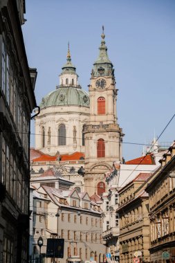 Prague, Czech Republic, 15 December 2022: View of Baroque Church of Saint Nicholas, green dome and bell tower with clock, sunny winter day, snow on red roofs, Mala Strana or Lesser Town district
