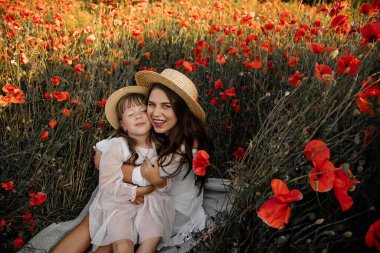 Haşhaş tarlasında kızıyla güzel bir genç kadın, beyaz elbiseli bir anne ve kız ve akşamleyin saman şapkalı yaz kırsal doğa çiçekleri, aile ferahlığı, basit kırsal yaşam.