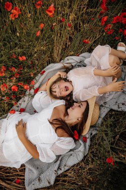 Haşhaş tarlasında kızıyla güzel bir genç kadın, beyaz elbiseli bir anne ve kız ve akşamleyin saman şapkalı yaz kırsal doğa çiçekleri, aile ferahlığı, basit kırsal yaşam.