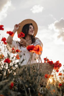 Kısa beyaz elbiseli ve saman şapkalı güzel bir kadın akşamları gelinciklerle birlikte tarlada ve elinde haşhaş, yaz kırsal doğa çiçekleri, kadın dinlendirici, kırsal basit hayat