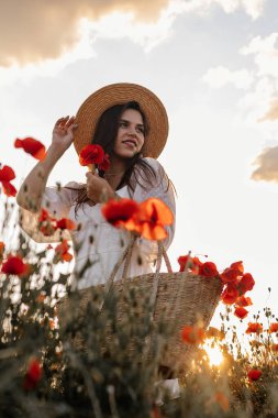 Kısa beyaz elbiseli ve saman şapkalı güzel bir kadın akşamları gelinciklerle birlikte tarlada ve elinde haşhaş, yaz kırsal doğa çiçekleri, kadın dinlendirici, kırsal basit hayat