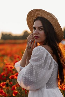 Kısa beyaz elbiseli ve saman şapkalı güzel bir kadın akşamları gelinciklerle birlikte tarlada ve elinde haşhaş, yaz kırsal doğa çiçekleri, kadın dinlendirici, kırsal basit hayat