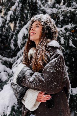 Kış tatili seyahati, Noel günü, yeni yıl, karlı ormanda güzel mutlu kadın portresi, doğa ormanı, kayak merkezi, eğlence aktivitesi, ladin dallarından düşen kardan hoşlanan genç bayan.