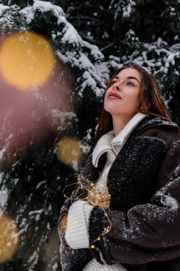 Kış tatili seyahati, Noel günü, yeni yıl, güzel mutlu kadın portresi karlı ormanlarda, doğa ormanlarında, kayak merkezlerinde, açık havada boş vakitlerde, genç bayan ellerinde çelenk ışıklarıyla eğleniyor.