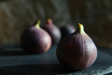 Siyah taştan bir tabakta mor incir, ayağa kalk. Taze sulu, olgun tropikal meyveler. Tam ve dilimlenmiş. Yemek fotoğrafı, arka plan. Vejetaryen ve çiğ, sağlıklı yiyecekler ve hasat için uygun. Sembol: