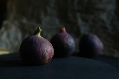 Siyah taştan bir tabakta mor incir, ayağa kalk. Taze sulu, olgun tropikal meyveler. Tam ve dilimlenmiş. Yemek fotoğrafı, arka plan. Vejetaryen ve çiğ, sağlıklı yiyecekler ve hasat için uygun. Sembol: