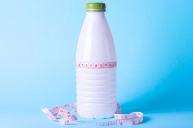 Spor yemekleri dengeli, kilolarını korumak ve kilo vermek için diyet yapmak için. Beyaz bir şişe yoğurt, süt, kefir, renkli bir arka plan ve bir santimetre mezura..
