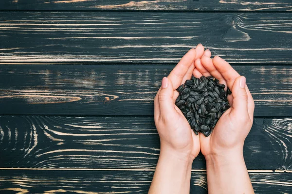 Sunflower seeds in female hands on a dark wooden background. Freshly harvested seeds, roasted seeds in a bunch
