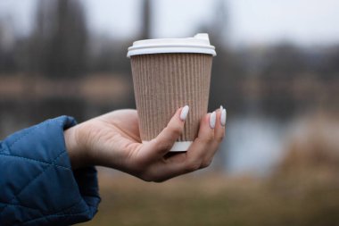 Doğada ekolojik kağıt bardaktan kahve içmek. Sıcak bir bardağı sıcak bir içecekle tutarken sıcak eller, sakinleşmek için yürüyüş..