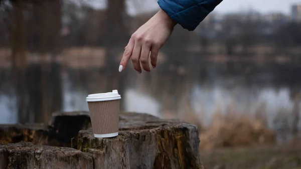 Drink coffee in nature from an ecological paper cup. Warming hands while holding a cup with a hot drink, walking as a way to calm down.