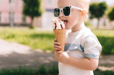 Küçük bir çocuğun portresi. Bir bebek lezzetli bir dondurma külahı yer. Mutlu çocuk. Yaz günü