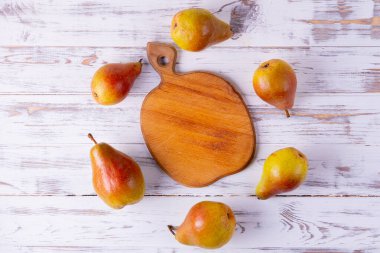 Tahta kesme tahtası altı olgun armutla çevrilidir, beyaz ahşap bir masanın üstünde daire şeklinde dizilmiştir..