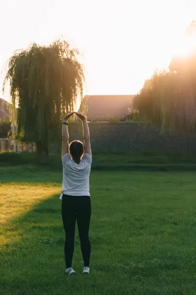 Günbatımının arka planında sportif bir kız ve doğa ellerini dağa uzatıyor. Temiz hava egzersizi yap. Yaz akşamı..