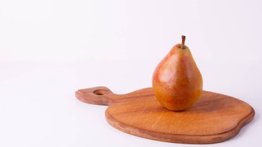 Tek, olgun bir armut, tahta bir kesme tahtasının üzerinde beyaz bir zemine karşı oturur..