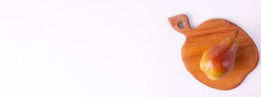 Tek bir kırmızı armut, beyaz arkaplana karşı duran tahta bir kesme tahtasının üzerinde duruyor..