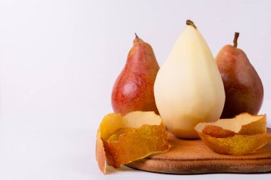 Üç armut, bir sarı ve iki kırmızı, yakınlarda kabukları olan bir tahta kesme tahtasının üzerinde otururlar..