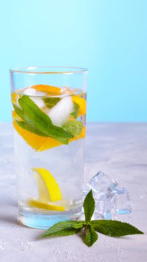 A glass of cold water with ice, lemon, and mint on a white table. clipart