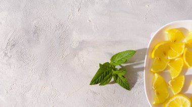 Beyaz bir tabakta taze limon dilimleri ve desenli beyaz arka planda bir nane filizi..