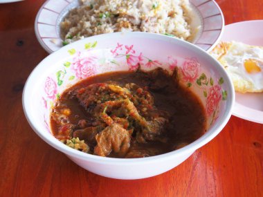 Balık ve yakın plan omlet ile ekşi körili Tayland çorbası, ahşap masa arkasına yerleştirilmiş beyaz bir kabın içinde lezzetli bir sıcak çorba. Malzeme olarak pilav ve kızarmış yumurta var..