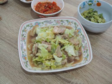 Tayland yemeği, tavada kızartılmış domuz göbeği ve marul. Arkaplan olarak diğer yiyeceklerle birlikte ahşap masaya yerleştirilmiş.