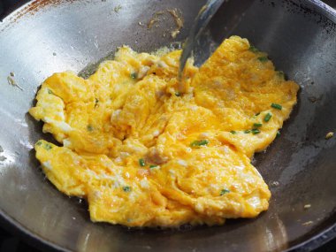 Kızartma tavasında doğranmış yeşil soğanlı taze pişmiş omlet, yemek yaparken bir spatula tarafından kaldırıldı. Basit ev yapımı Asya usulü kahvaltı..
