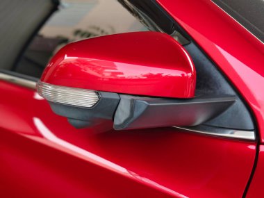 Siyah üsse monte edilmiş, entegre dönüş sinyalli, parlak kırmızı araba yan aynası. Yansımalar kentsel çevre ve modern tasarım öneriyor.