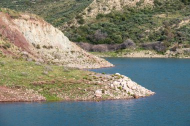 Kıbrıs Rum Kesimi Peyia 'daki Mavrokolympos rezervuarının yeşil kayalık tepeleri ve mavi suyu