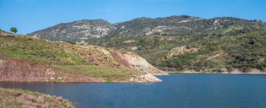 Mavrokolympos rezervuarı üzerinde mavi su ve kayalık yeşil dağlar, Peyia, Kıbrıs Rum Kesimi üzerinde geniş panoramik manzara