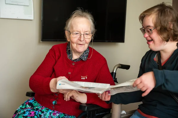 Happy moment between an 85 yo mother reading a newspaper with her daughter with the Down Syndrome, Tienen, Flanders, Belgium