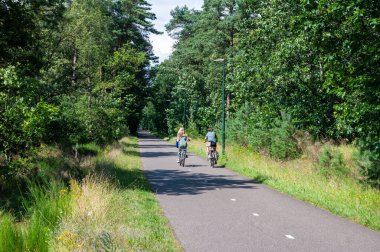 Heeze, Kuzey Brabant, Hollanda, 10 Temmuz 2024 - Groote Heide doğa koruma alanında bisiklet yolunu kullanan anne ve genç kız