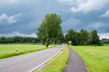 Neuenhaus, Niedersachsen, Almanya, 13 Temmuz 2024 - Ootmarsumer sokağı, bulutlu gökyüzüne karşı bisiklet yolu