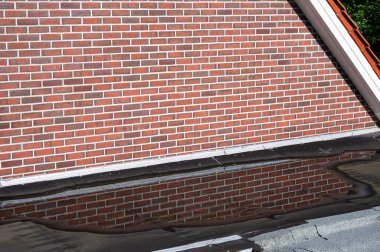 Osterwald, Lower Saxony, Germany -  July 14, 2024 - Brick stone wall and rooftop reflecting in water of a residential house clipart