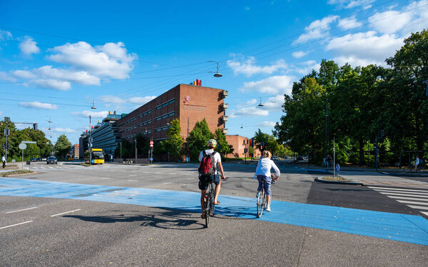 Copenhagen, Denmark, July 24, 2024 - Cyclists at a cross with the unievrsity of Copenhagen int he background