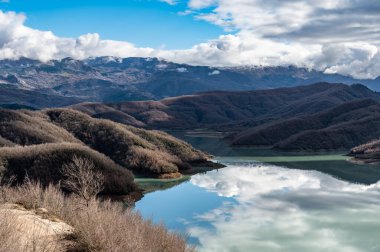 Arnavutluk 'taki Gamti Dağı ve Bovilla Gölü' nün yüksek açılı manzarası. Yapay gölün mavi sularıyla gri ve yeşil kaya oluşumu ve arka planda dağlar..