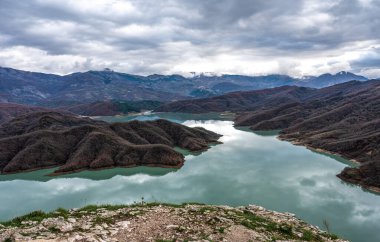 Gamti dağları ve Bovilla Gölü 'nün üzerindeki manzara panoramik. Renkli bir besin, mavi su ve bulutlu bir gökyüzü olan Arnavutluk.