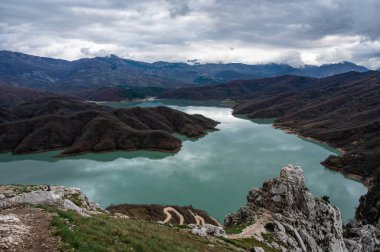 Scenic panoramic view over the Gamti mountains and Bovilla lake with colorful begetation, blue water and an overcast sky, Albania clipart