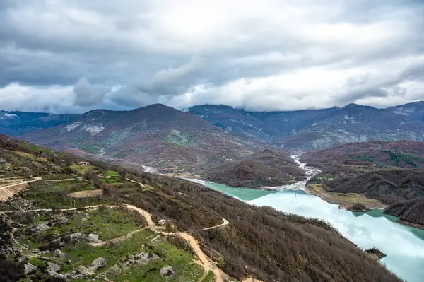 Arnavutluk 'taki Gamti Dağı ve Bovilla Gölü' nün yüksek açılı manzarası. Yapay gölün mavi sularıyla gri ve yeşil kaya oluşumu ve arka planda dağlar..
