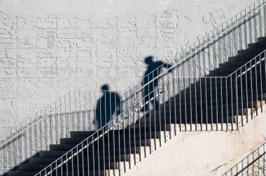 Çağdaş bir merdiven ve sert güneş ışığıyla kavramsal çalışma. Arnavutluk 'un Tiran kentinde merdivenlerden inen insanların gölgeleri. 13 Aralık 2024