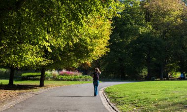 Schaerbeek, Brüksel - Belçika - 10: 15 2018 Sıcak bir sonbahar gününde parkta yürüyen genç bir kadın. Model bırakıldı