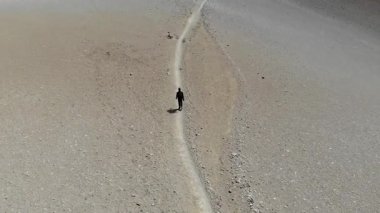 Kamera, çorak toprağa oyulmuş dar bir yolda yürüyen yalnız bir dağcıyı nazikçe takip eder. Her adım bu engin yüksek irtifa çölünün sessizliğini yansıtıyor..
