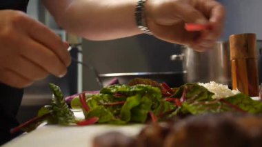 Bu video, taze yeşil sebzeler kullanarak sağlıklı bir yemek hazırlayan bir şefi çekiyor. Tezgahta, yapraklı yeşiller ve öğütülmüş malzemeler pişirmek için hazırken, arka plandaki bir tencereden buhar yükseliyor..
