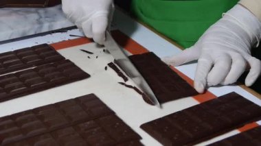 Bu video, ambalajdan hemen önce çikolata fabrikasında yeni yapılmış çikolatalara dokunan bir işçiyi gösteriyor. % 100 saf kakaodan yapılmıştır. Parmaklıklar kenarları budandığı için temiz bir yüzeye serilmiştir..