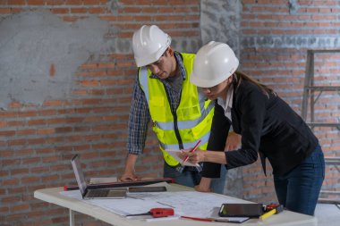 Güvenlik teçhizatı inceleme planlarını inceleyen iki inşaat mühendisi dizüstü bilgisayarlar ve belgelerle proje planlarını tartışıyorlar..