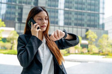 Meşgul bir iş kadını dışarıda telefonla konuşurken zamanı kontrol ediyor.