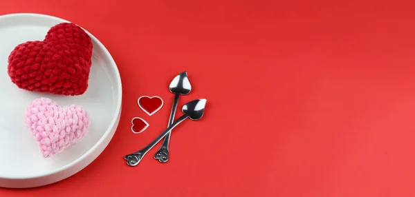 Saint Valentine Day background. Food concept for a romantic dinner on red background. Creative image of valentine hearts served on plate with heart shaped spoons and hearts nearby. Copy space for text. Red and pink hearts served on a white plate