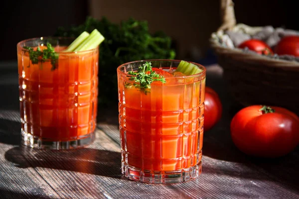 stock image tomato juice close up with fresh tomatoes and basil on a dark background. two glasses of bloody mary cocktail with fresh celery and parsley on a wooden table in natural lightning, rustic style. Fresh vegetable juice with tomatoes