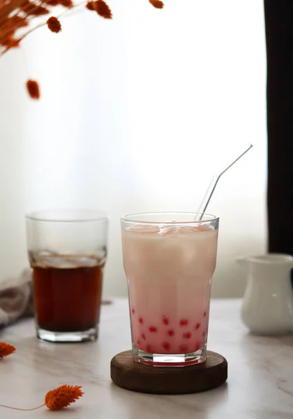 Home made milk bubble tea with tapioca pearls. Strawberry iced milk tea drink with tapioca balls. Milky drink with tapioka bubbles and ice. Bubble tea or boba tea on a table, home interior