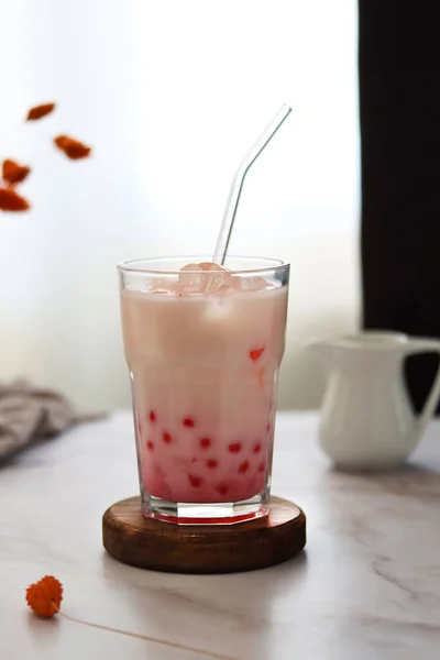 Homa made iced milk bubble tea with tapioca pearls. Strawberry milk tea drink with tapioca balls. Milky drink with tapioka bubbles and ice. Bubble tea or boba tea on a table, home interior