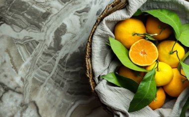 Yeşil yapraklı mermer zemin üzerinde bir sepette Türk sarısı yeşil mandalinaları, masada yarısı dilimlenmiş mandalinalar, kırsal arka plan. Boşluğu kopyala